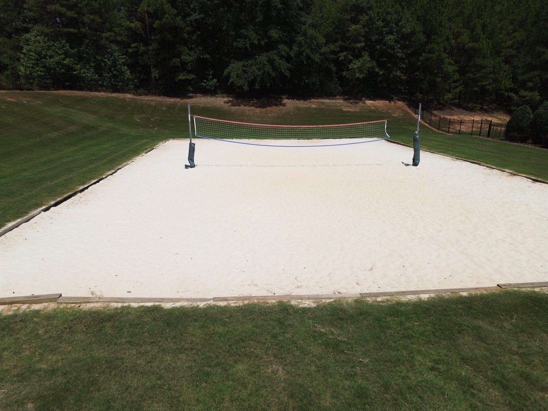 Community sand volleyball court beside a wooded green space